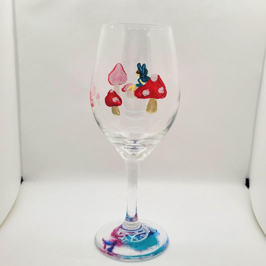 Hand-painted 12 oz dessert wine glass featuring a blue-winged fairy surrounded by red mushrooms by Amy Bridges