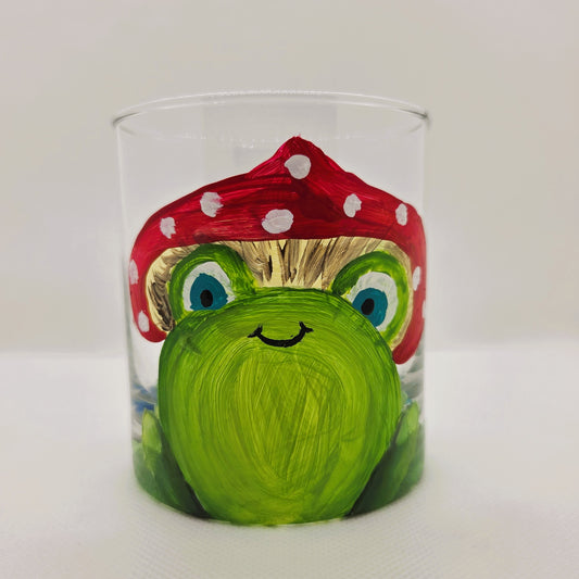 Hand-painted 11 oz highball glass featuring a whimsical frog sitting on a lily pad wearing a red mushroom hat with lily pad details wrapping around the glass.