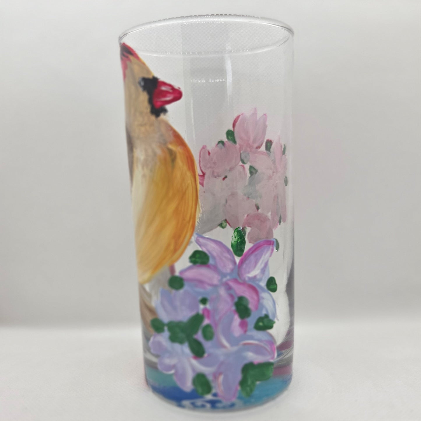 Hand-painted 16 oz tall tumbler with a female cardinal perched on a flowering branch surrounded by red, white, blue, and pink blossoms