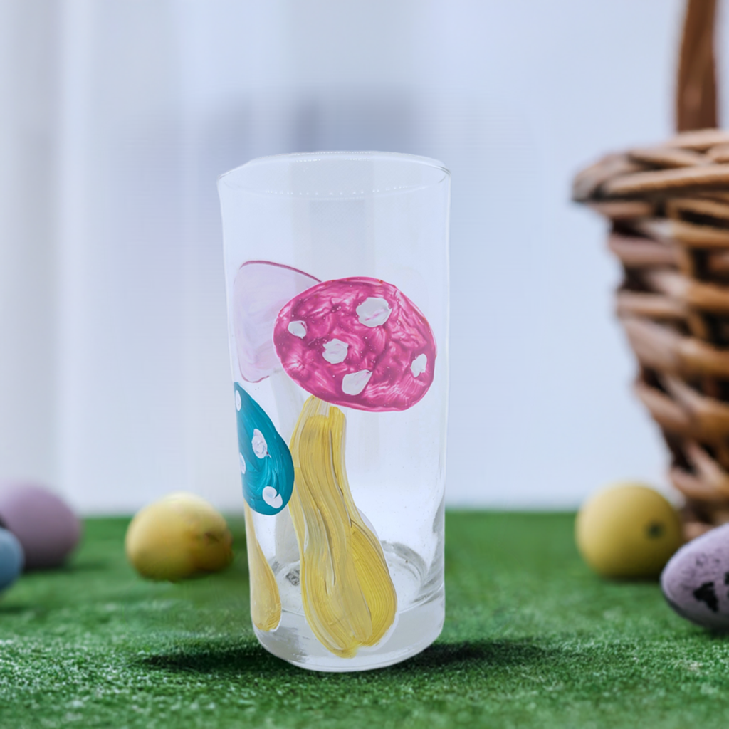 Hand painted 16 oz glass tumbler featuring three colorful mushroom designs in magenta, blue, and pink, whimsical functional art glassware by Amy Bridges.