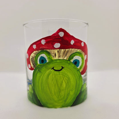Hand-painted 11 oz highball glass featuring a whimsical frog sitting on a lily pad wearing a red mushroom hat with lily pad details wrapping around the glass.