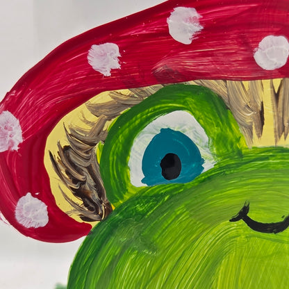 Hand-painted 11 oz highball glass featuring a whimsical frog sitting on a lily pad wearing a red mushroom hat with lily pad details wrapping around the glass.