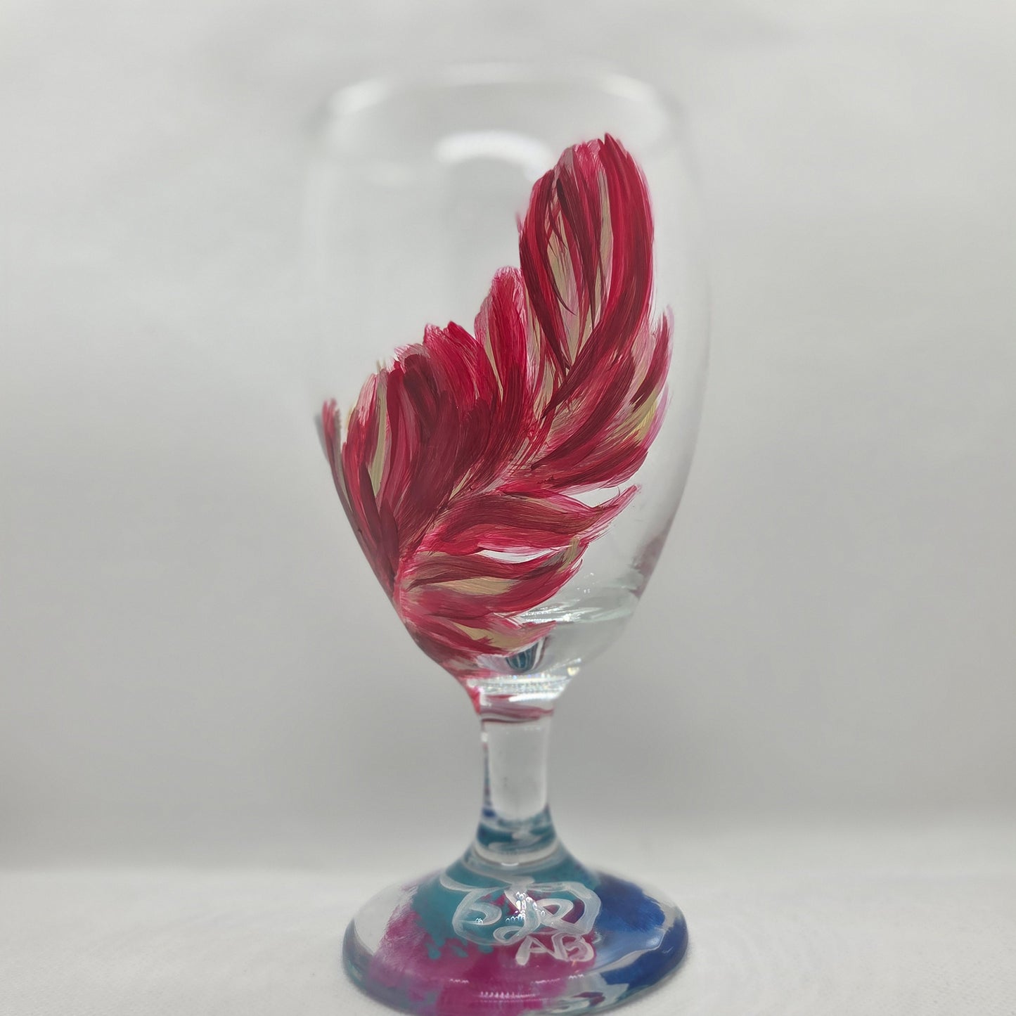 Hand-painted 16 oz glass with a graceful cardinal feather in brilliant red, orange, and golden yellow